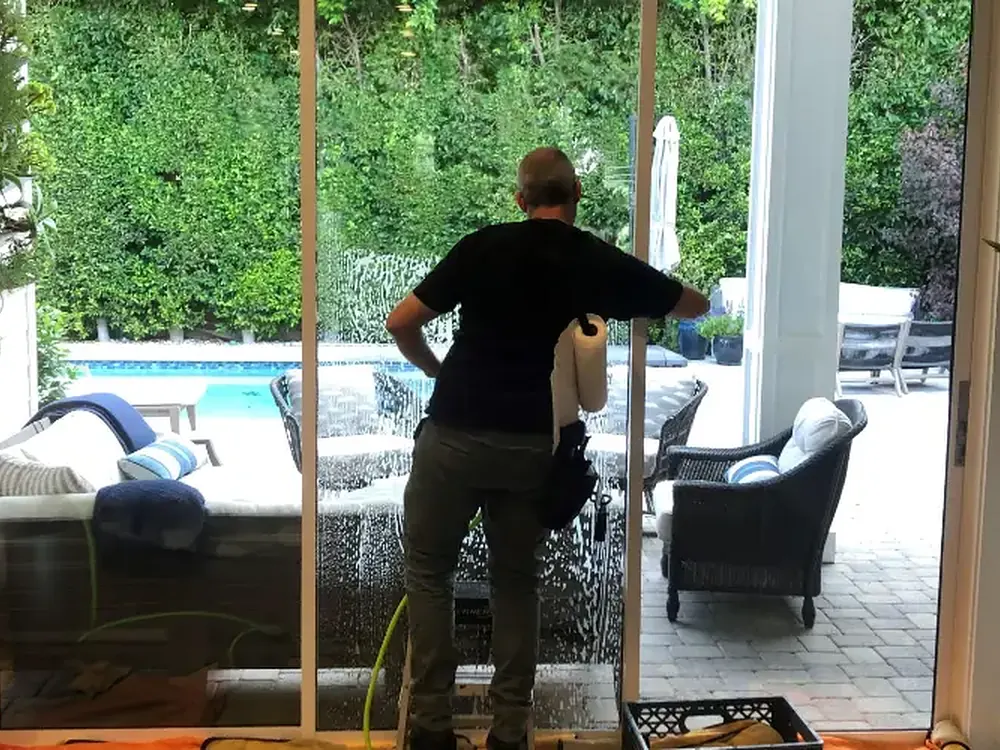 An installer working security film down onto a sliding glass door overlooking a pool.